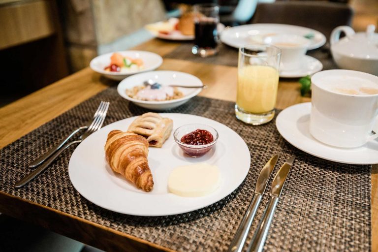 Detailaufnahme eines süßes Frühstücks im Restaurant RIVA im Weinhotel Kaisergarten Deidesheim/ Pfalz. Buttercroissant, Kirschtasche, Marmelade und Butter, angereichtet auf einem weißen Teller. Daneben Saftglas, Kaffeetasse und Müslischälchen.