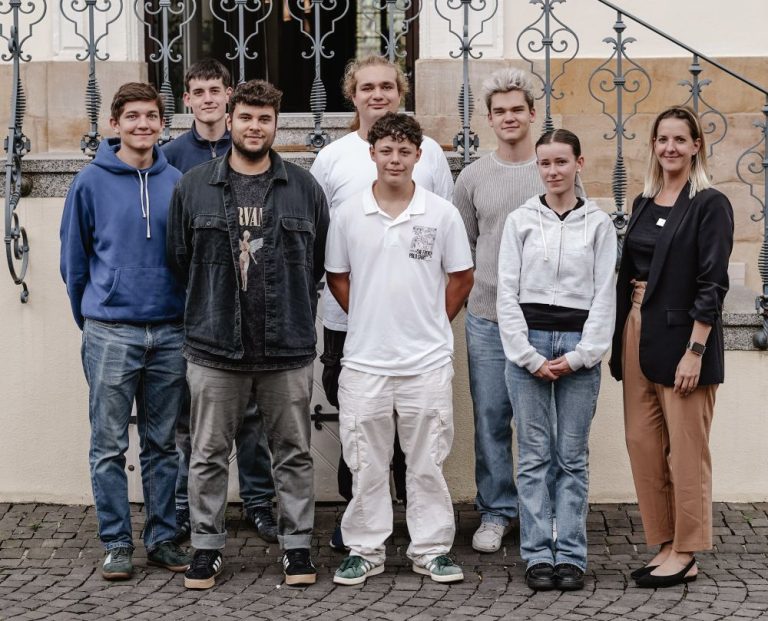 Wir heißen unsere neu startenden Auszubildende willkommen! Auf dem Foto sieben Azubis in zwei Reihen zusammen mit Personalreferentin Nicole Hochgesang. Die Gruppe steht vor dem Hoteleingang unseres Boutiquehotels Ketschauer Hof, Deidesheim Pfalz.